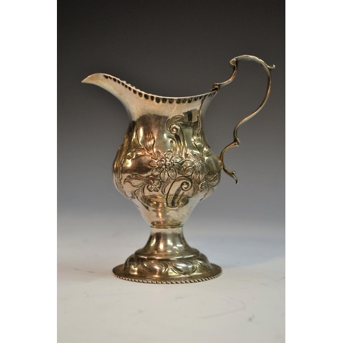 698 - A George III silver pedestal cream jug, embossed and engraved with foliate scrolls, vacant cartouche... 