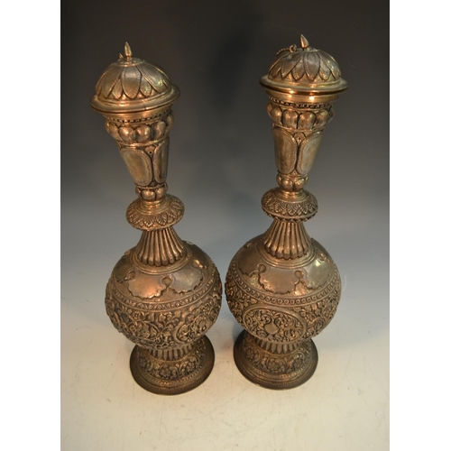 763 - A pair of Indian Kutch silver baluster rose water flasks, domed lotus covers, profusely chased and e... 