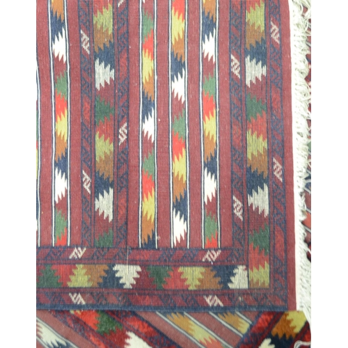 1744 - A Turkish kilim, with geometrical bands, in brown, red, green and cream on a red ground, 182cm x 120... 