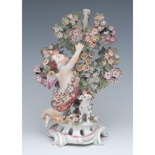 72 - A Bow figure, Cupid, the winged putto kneeling and reaching up into flowering bocage with a lamb bes... 