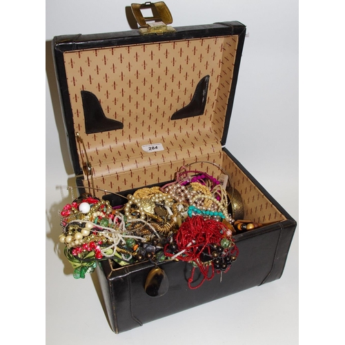 284 - A black leather vanity case containing mid 20th century costume jewellery including faux pearl, bead... 