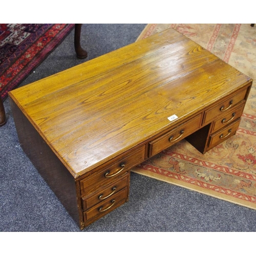 135 - A low elm pedestal desk with an arrangement of seven drawers