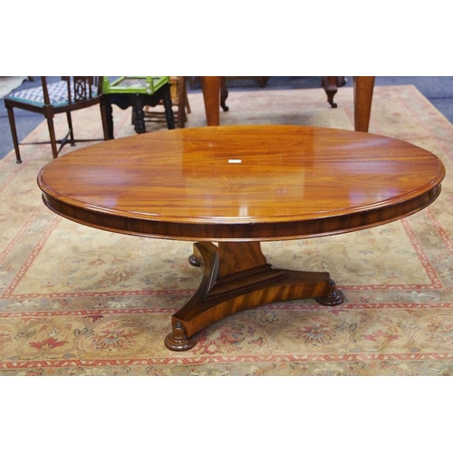 137 - A mahogany oval coffee table, triangular column, incurved trefoil base, bun feet