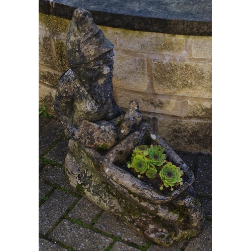 334 - A reconstituted stone garden gnome pushing a wheelbarrow, 70cm high