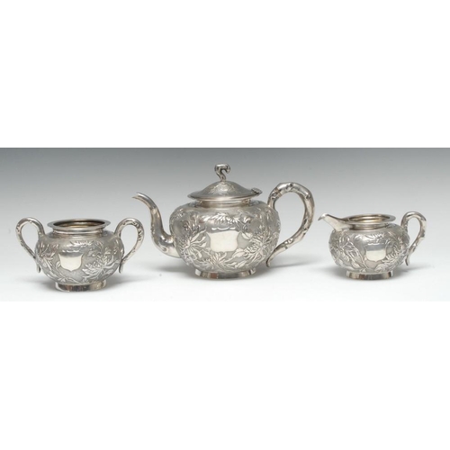 575 - A Chinese silver three piece tea service, comprising teapot, milk jug and sugar basin, each chased w... 