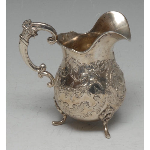 579 - A Continental Rococo silver helmet shaped cream jug, chased with ho-ho type bird song C-scrolls and ... 