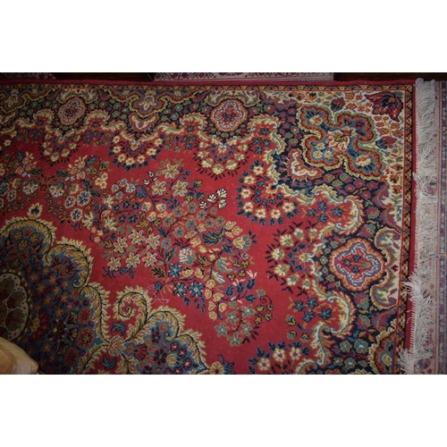 463 - An Oriental style carpet, decorated with stiff, scrolling and whiplash stems and foliage on a crimso... 