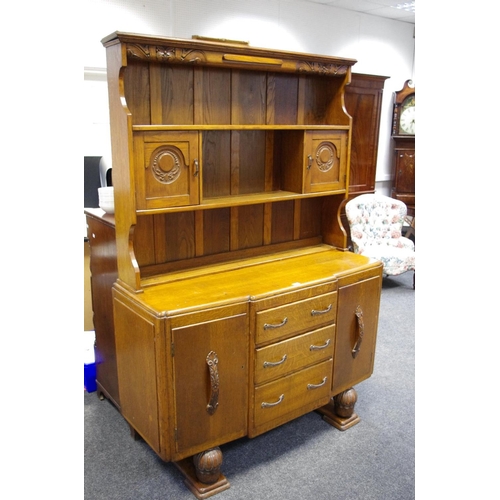 186 - A 1930's oak breakfront dresser, two cupboards and shelving to carved top, three drawers flanked by ... 