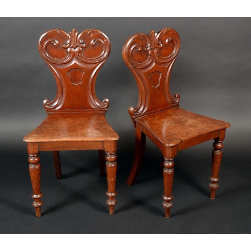 1438 - A pair of Victorian mahogany hall chairs, shaped backs carved with scrolling acanthus and centred by... 