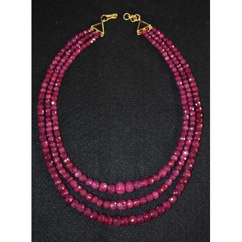 3207 - A three strand faceted ruby bead necklace, three tapering graduated strands of pinky red rubies rang... 