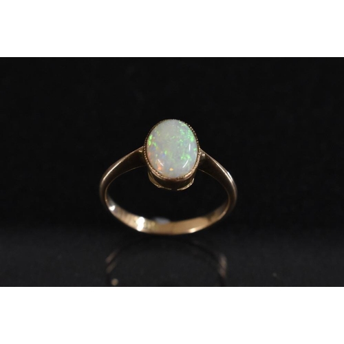 3226 - An 18ct gold ring, set with a single polished oval opal cabochon, flashing green, violet and orange ... 