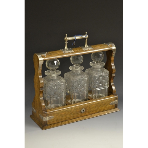 5188 - A Victorian EPNS mounted oak three-bottle tantalus, canted square decanters hobnail cut to waist, pr... 