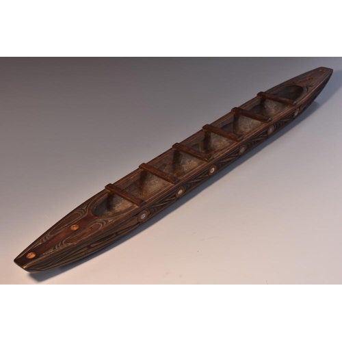 3854 - Tribal Art - a Maori model waka canoe, carved with stylised motifs and inlaid with abalone roundels,... 