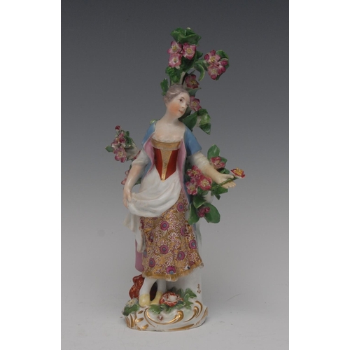 67 - A Chelsea figure, of a lady, standing holding a flower posy, wearing a floral skirt, before bocage, ... 