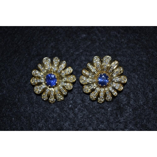 3475 - A pair of sapphire and diamond floral ear clips, central circular blue sapphire, surrounded by a tex... 