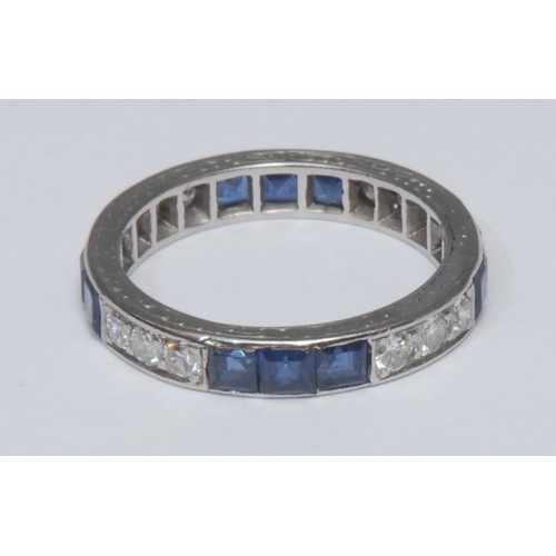 816 - A sapphire and diamond eternity ring, channel set wit alternating clusters of three square cut blue ... 