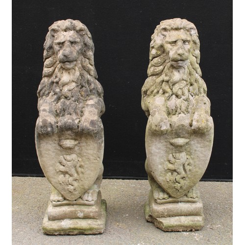 1555 - A pair of reconstituted stone heraldic lions, each grasping a shield, stepped bases, 81cm high, 26cm... 