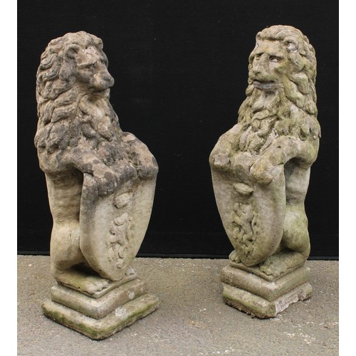 1555 - A pair of reconstituted stone heraldic lions, each grasping a shield, stepped bases, 81cm high, 26cm... 