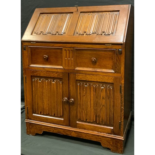 258 - A mid 20th century oak bureau, linen fold fall front, above frieze drawer and pair of cupboard doors... 