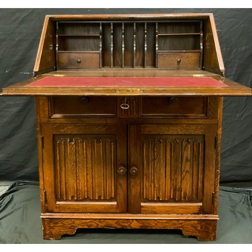 258 - A mid 20th century oak bureau, linen fold fall front, above frieze drawer and pair of cupboard doors... 