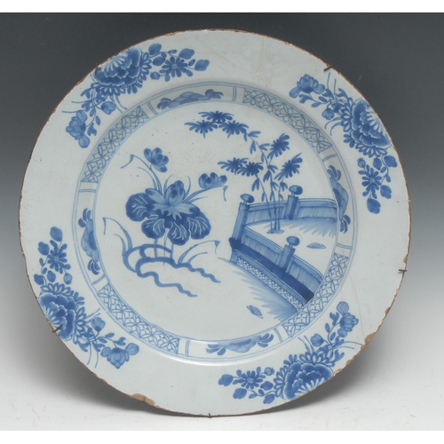 445 - An English 18th century Delft charger, decorated in underlaze blue with stylised flowers and fence, ... 