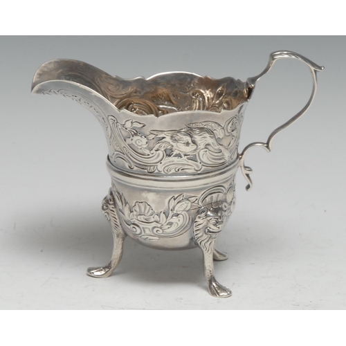 308 - An Irish silver helmet shaped cream jug, chased in the Rococo taste with scrolling leaves and birds,... 