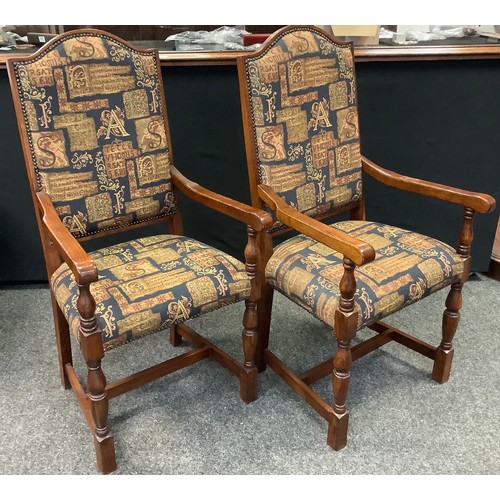 101 - A pair of 21st century oak elbow chairs, the arched back and seats upholstered in Medieval style tap... 