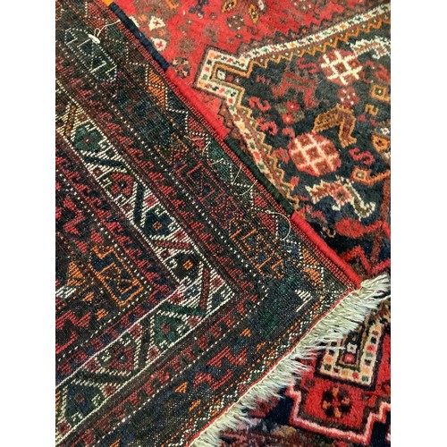 252 - An early to mid 20th century Persian Shiraz wool rug, hand-knotted in deep red, the central field wi... 