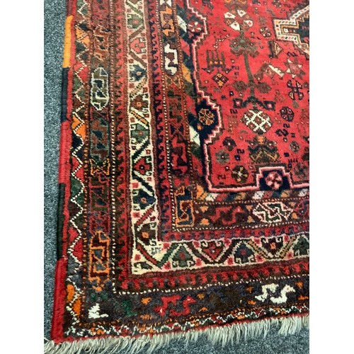 252 - An early to mid 20th century Persian Shiraz wool rug, hand-knotted in deep red, the central field wi... 