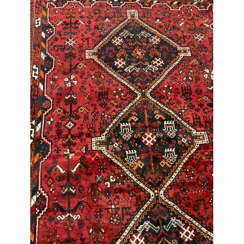 252 - An early to mid 20th century Persian Shiraz wool rug, hand-knotted in deep red, the central field wi... 