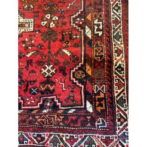 252 - An early to mid 20th century Persian Shiraz wool rug, hand-knotted in deep red, the central field wi... 