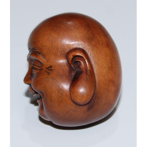 5168 - A Japanese boxwood netsuke, carved as the head of Buddha, smiling, 4cm long, signed