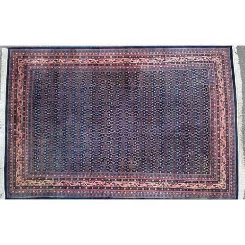 650 - A large Persian style woollen carpet, woven with geometric patterns in shades of red, ochre and oran... 