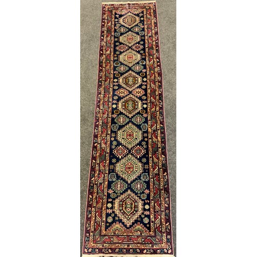 136 - A hand-made Heriz runner carpet, woven with stylised geometric motifs in shades of red, pale green, ... 
