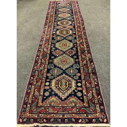 136 - A hand-made Heriz runner carpet, woven with stylised geometric motifs in shades of red, pale green, ... 