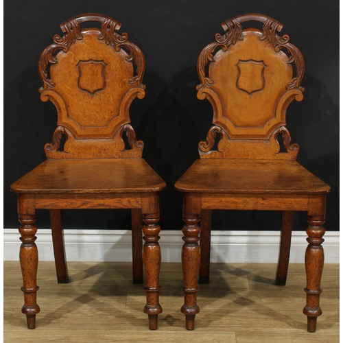 12 - A pair of late Victorian oak hall chairs, each with a shaped back carved with leaves and centred by ... 