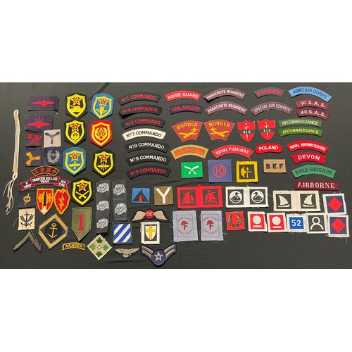 173 - A collection of reproduction British cloth insignia, reproduction Waffen SS deathshead cap insignia ... 