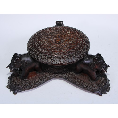 5273 - An Indian hardwood table top vase stand, the circular plateau on four elephant supports, triform bas... 