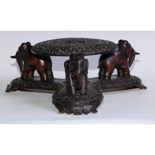 5273 - An Indian hardwood table top vase stand, the circular plateau on four elephant supports, triform bas... 