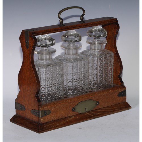 5137 - A late Victorian/Edwardian oak three-bottle tantalus, arched carrying handle, hobnail-cut square gla... 