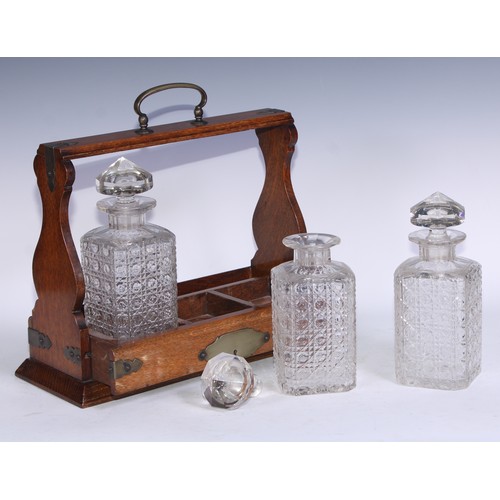 5137 - A late Victorian/Edwardian oak three-bottle tantalus, arched carrying handle, hobnail-cut square gla... 