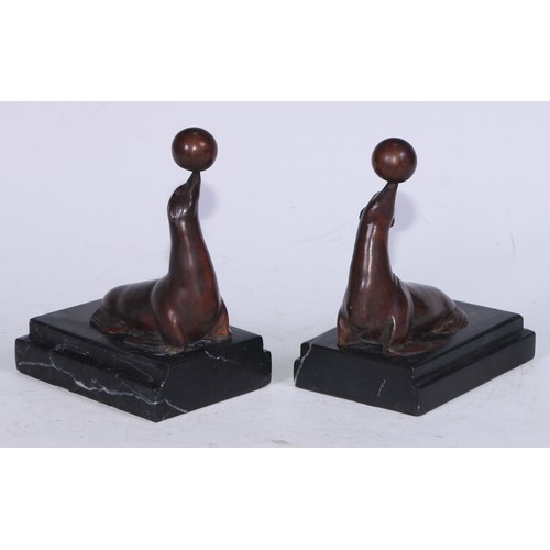 5171 - A pair of Art Deco design brown patinated bronze bookends, each cast with a seal balancing a ball, s... 