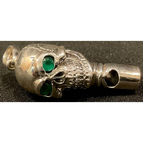 225 - A silver novelty whistle, as a skull, emerald eyes, 4.5cm long