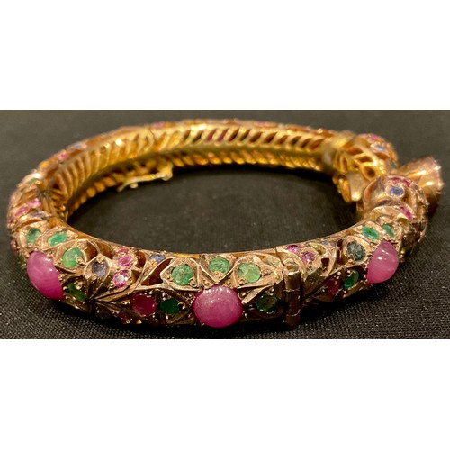 461 - A gold plated hinged pierced openwork bangle encrusted overall with low grade cabochon rubies and fa... 