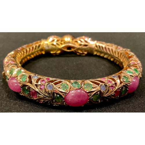 461 - A gold plated hinged pierced openwork bangle encrusted overall with low grade cabochon rubies and fa... 