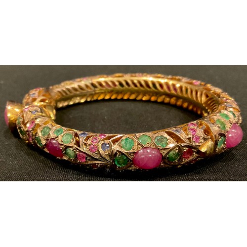 461 - A gold plated hinged pierced openwork bangle encrusted overall with low grade cabochon rubies and fa... 