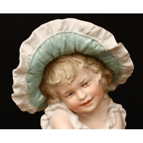 3298 - A Gebrüder Heubach (Germany) bisque piano baby, of a seated young girl, wearing a large bonnet and d... 