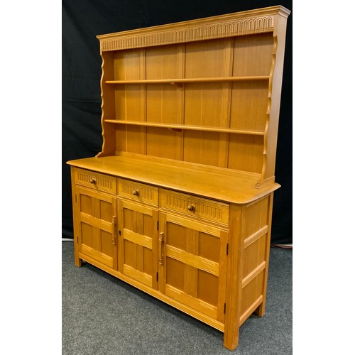 258 - An Ercol style light oak dresser, the top with two tiers of shelving, above a base with three short ... 