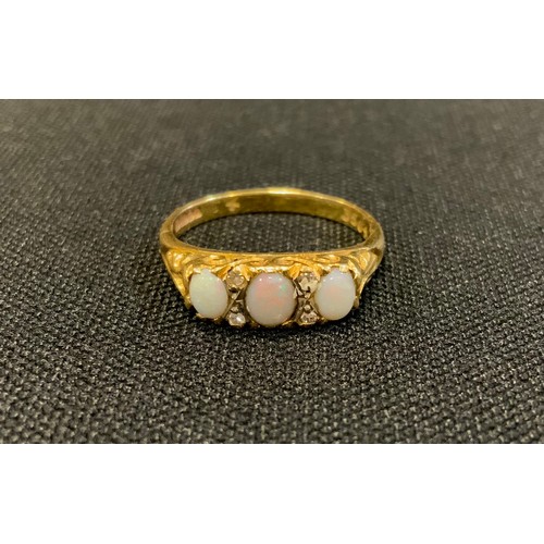 721 - A diamond and opal ring, set with three oval opal cabochons each divided by a pair of diamond accent... 