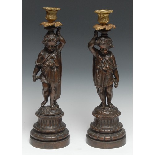 185 - A pair of sculptural 19th century French bronzed and parcel-gilt figural candlesticks, each cast as ... 